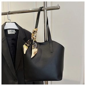 Detail of a black matte leather tote bag with a vintage patterned silk scarf on the handle
