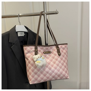 Detail of pink plaid tote bag featuring long brown leather handles and plush bear charm