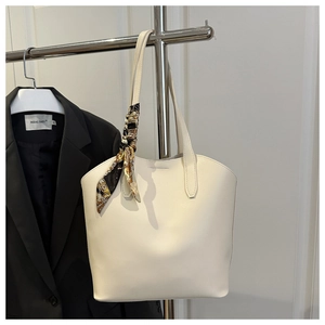 Close-up of cream leather tote bag featuring a decorative printed silk scarf on the handle