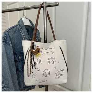 Detail of white canvas tote bag featuring brown leather straps and cute cartoon cat graphics