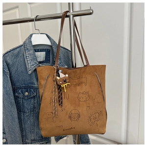 Close-up of brown faux suede tote bag with cartoon cat prints and bear plush charm