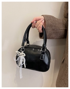 Close-up of small black bowling handbag with delicate white lace bow and pearl charm