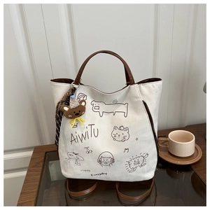 Detail of canvas tote bag featuring whimsical cat illustrations and a brown plush bear charm