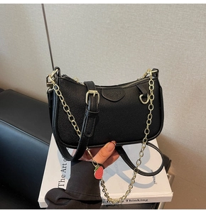 Detail of black pebbled leather half-moon bag with gold chain and strawberry charm