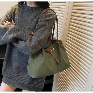 Detail of dark green faux suede tote bag with brown leather straps in indoor natural light