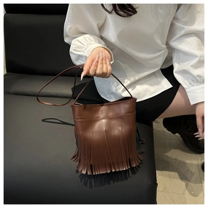 Detail view of dark brown tassel bucket bag in PU leather with long fringe and slim strap