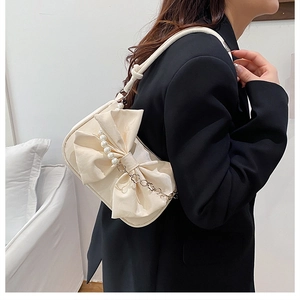 Detail of cream crossbody bag featuring a large bow, pearl accents, and knot strap