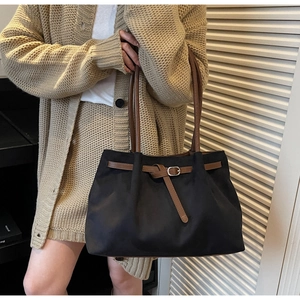 Close-up of black matte tote bag featuring brown leather straps and metal buckle detail