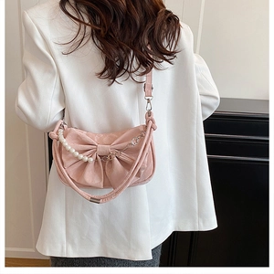 Detail of pink bow-shaped shoulder bag with pearl strap worn by a model in casual blazer