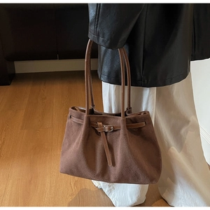 Deep brown suede tote bag shown on model with shoulder strap and metal buckle detail