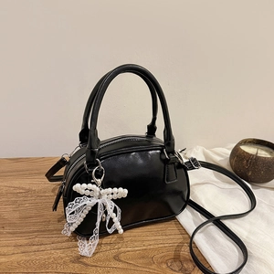Minimalist black bowling handbag with pearl bow charm on a natural wood surface