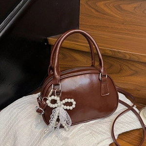 Retro brown bowling handbag in polished PU leather with pearl bow charm on white fabric