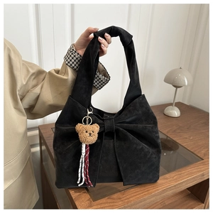 Detail of black suede tote bag with large bow and brown plush bear charm