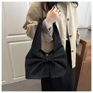 Close-up of black oversized bow detail on suede shoulder bag with wide strap