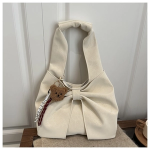 Detail of cream tote bag featuring a large bow decoration and brown plush bear charm
