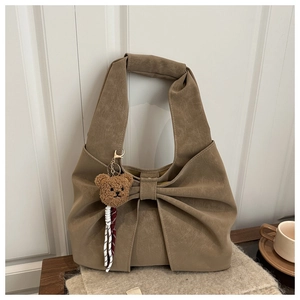 Detail of coffee brown suede tote bag featuring a decorative bow and plush bear charm