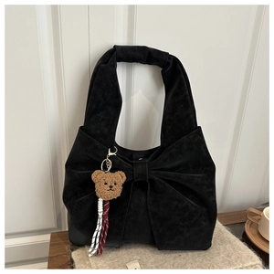Detail of black suede tote bag with large bow design and brown plush bear charm