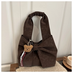 Detail view of brown suede tote with large bow accent and plush bear charm on a table