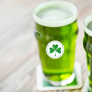 Green St. Patrick's Day beer in glass with clover sticker on light wood background