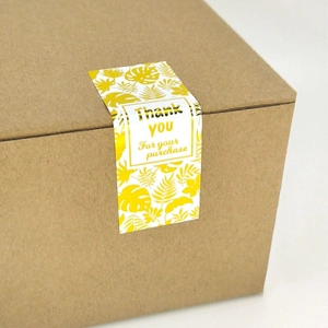 White rectangular gold foil Thank You stickers with tropical leaf patterns on a box