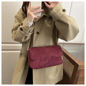 Detail view of burgundy suede flap bag with elegant gold chain strap on a khaki trench coat