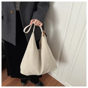Detail of beige large tote bag with wooden bead pendant worn with a dark coat