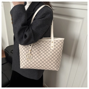 Close-up of beige tote bag canvas with M-letter pattern and golden metal pendant detail