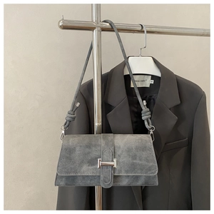 Detalle de bolso de ante gris con nudo en correa y hebilla plateada en una percha
