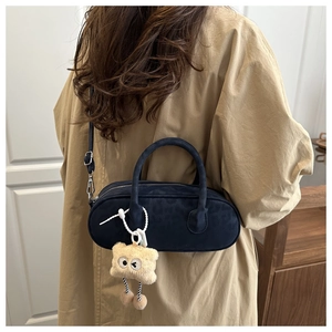 Navy blue suede pillow bag with plush charm shown from side view on trench coat model