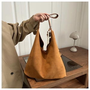 Detail of caramel brown suede tote bag with decorative wooden beads on a desk