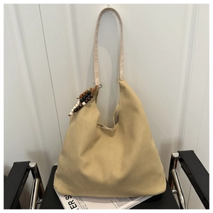 Close-up of beige suede tote bag with colorful wooden bead charm on a black chair