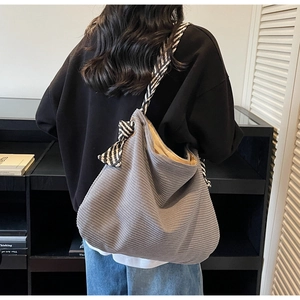 Detail showing grey corduroy tote bag texture with striped ribbon shoulder strap on model