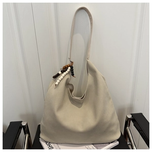 Detail of beige hobo tote bag on chair featuring colorful wooden bead charm and wide strap