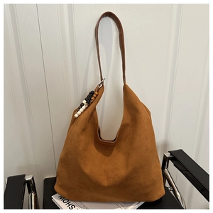 Detail of a large brown suede hobo bag with unique decorative wooden beads on a black chair