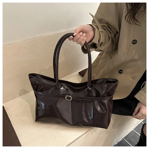 Détail du sac seau marron foncé brillant avec boucle dorée et texture en cuir lisse