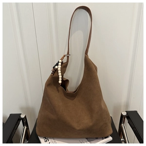 Detail of a large brown suede hobo bag with leather strap and wooden bead charm on a chair