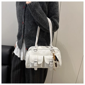Detail of white patent leather shoulder bag with flap pockets and wooden bead charm