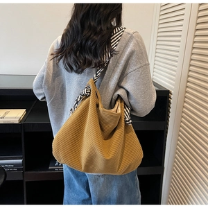 Detail of corduroy tote bag featuring striped wide shoulder strap tied to metal eyelet