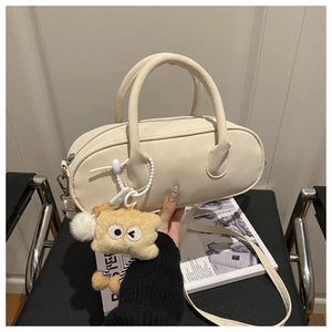 Detail of a chic cream cylindrical pillow bag featuring a fuzzy brown monster charm