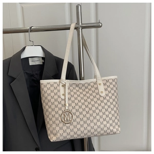 Close-up of cream monogram tote bag with gold M pendant and slim shoulder strap