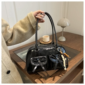 Detail of black glossy bow handbag with wooden bead charm on a wooden desk setup
