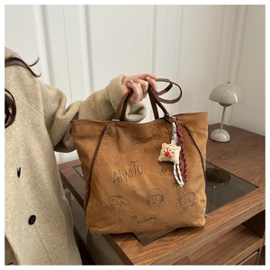Detailed view of brown suede tote with cat graffiti, plush charm, and braided strap