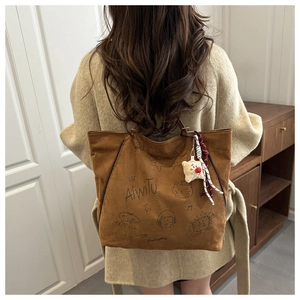 Détail du sac cabas en daim marron avec graffitis et breloque étoile sur le mannequin