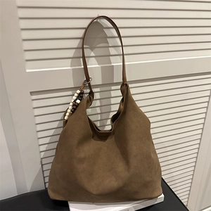 Brown suede tote bag with minimalist design and stylish beaded charm hanging from the strap