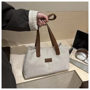 Détail du sac cabas en toile avec poignées en cuir marron et écusson décoratif texturé