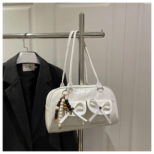 Detail of white patent leather shoulder bag with decorative bows and wooden bead charm