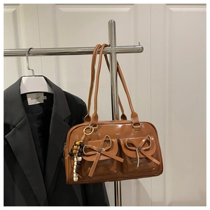 Detail of a glossy brown bowling bag featuring bow accents and a beaded tassel charm
