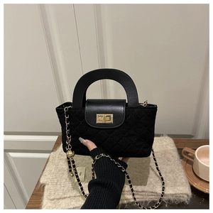 Detailed view of black quilted crossbody bag featuring gold twist lock and chain strap
