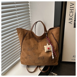 Detail of brown suede tote with black illustrations and plush pendant accessory