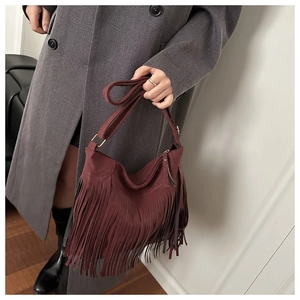Detail of burgundy fringe crossbody bag in matte suede held by model in a chic room